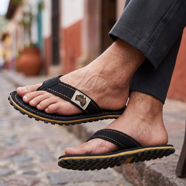 GUMBIES FRANCE Classic Black canvas flip-flops with tan stitching and a textured rubber sole.