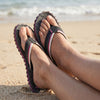GUMBIES FRANCE black and pink flip-flops with recycled rubber sole and cotton straps on a sandy beach.